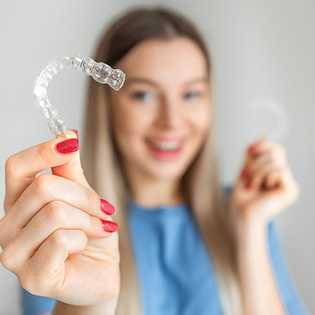 Woman smiling while holding two Invisalign aligners