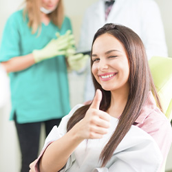 Smiling woman in dental chair winking and giving thumbs up