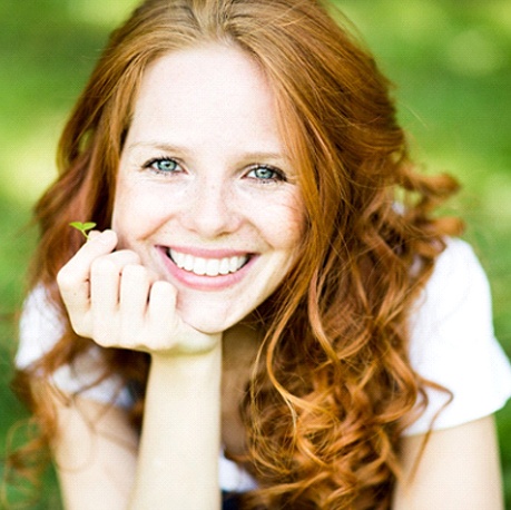 A young female with red hair holding a tiny leaf while embracing her new and improved smile