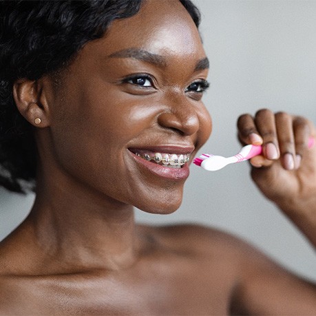 Woman with braces smiling while brushing their teeth